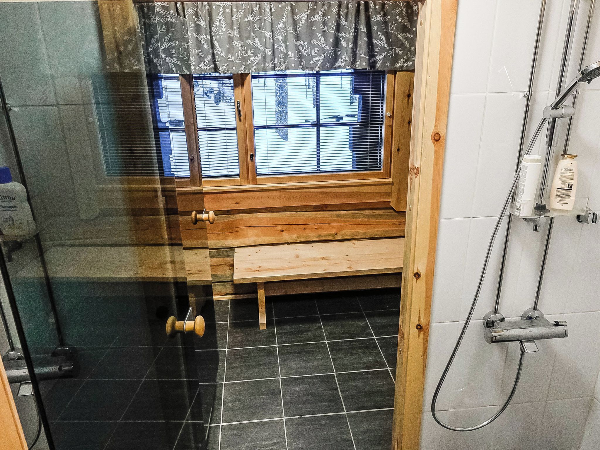 A bathroom with a shower, a bench, and a window with blinds.