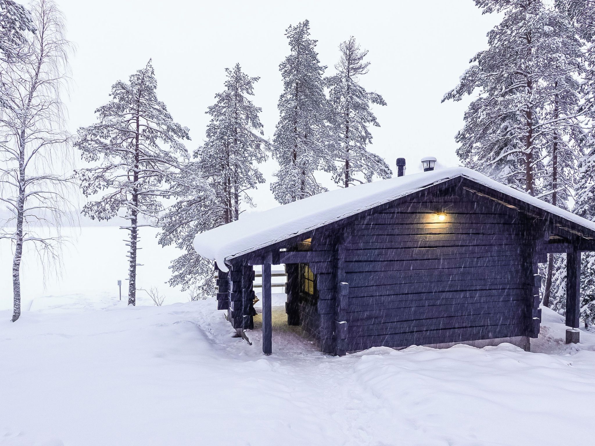Una cabaña de madera con tejado nevado, rodeada de árboles cubiertos de nieve.
