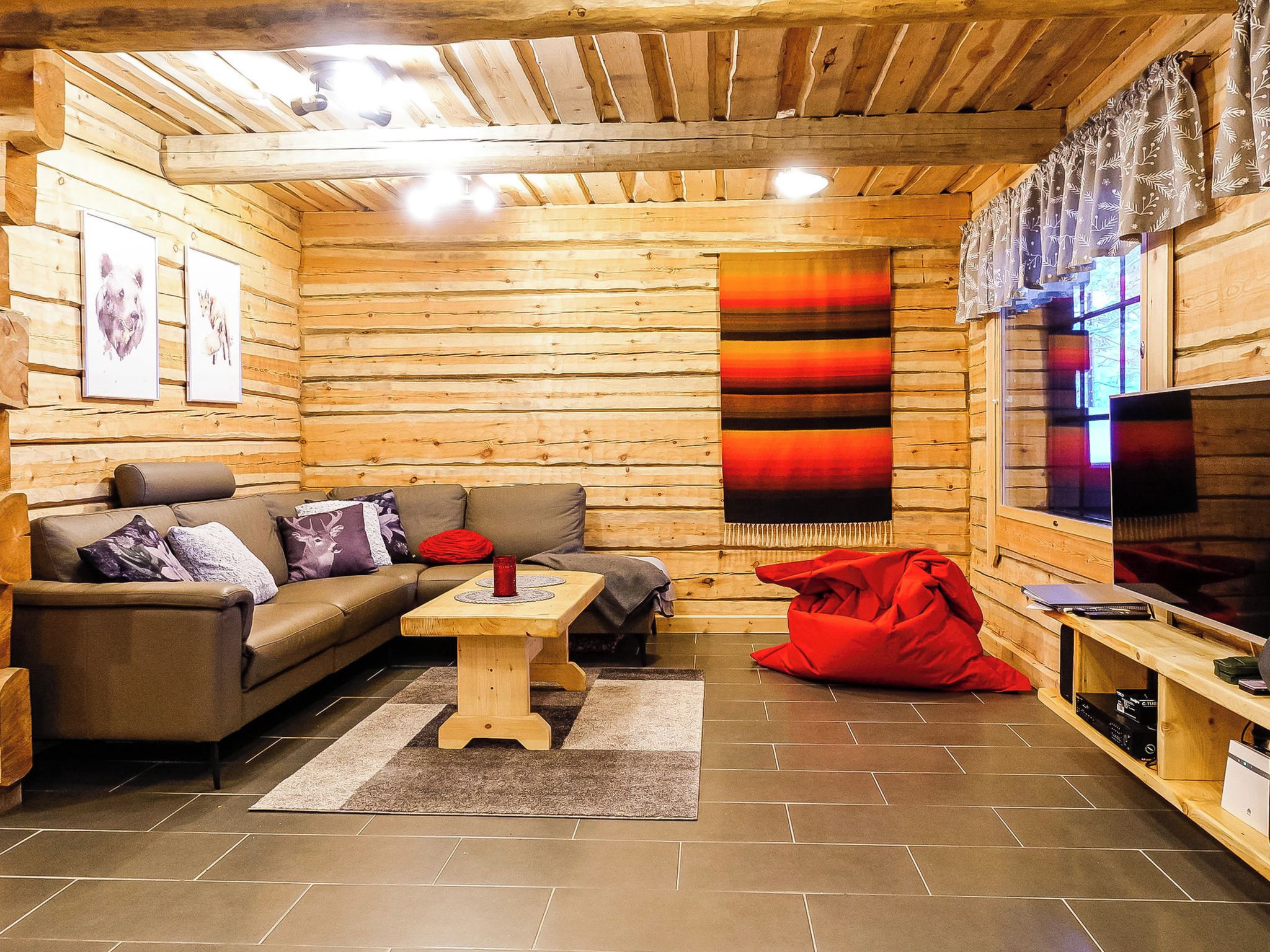 A cozy log cabin interior with a sofa, a coffee table, a red bean bag, and a television.