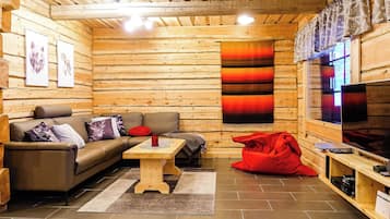 Interior acollidor d'una cabana de fusta amb un sofà, una taula de cafè, un seient de sac vermell i una televisió.