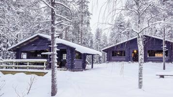 A cabin with a wooden exterior, surrounded by snow-covered trees, and a bench in the foreground.