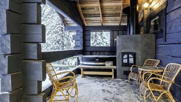L’intérieur d’une cabane en rondins, avec une cheminée en pierre, des meubles en osier et une vue sur des arbres couverts de neige.
