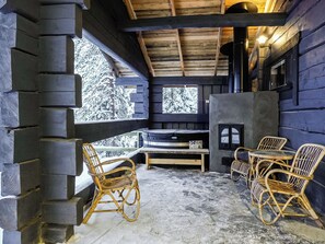 L’intérieur d’une cabane en rondins, avec une cheminée en pierre, des meubles en osier et une vue sur des arbres couverts de neige.