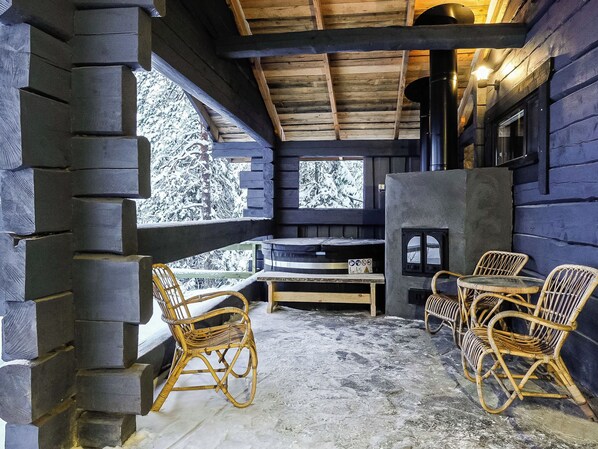 L’intérieur d’une cabane en rondins, avec une cheminée en pierre, des meubles en osier et une vue sur des arbres couverts de neige.