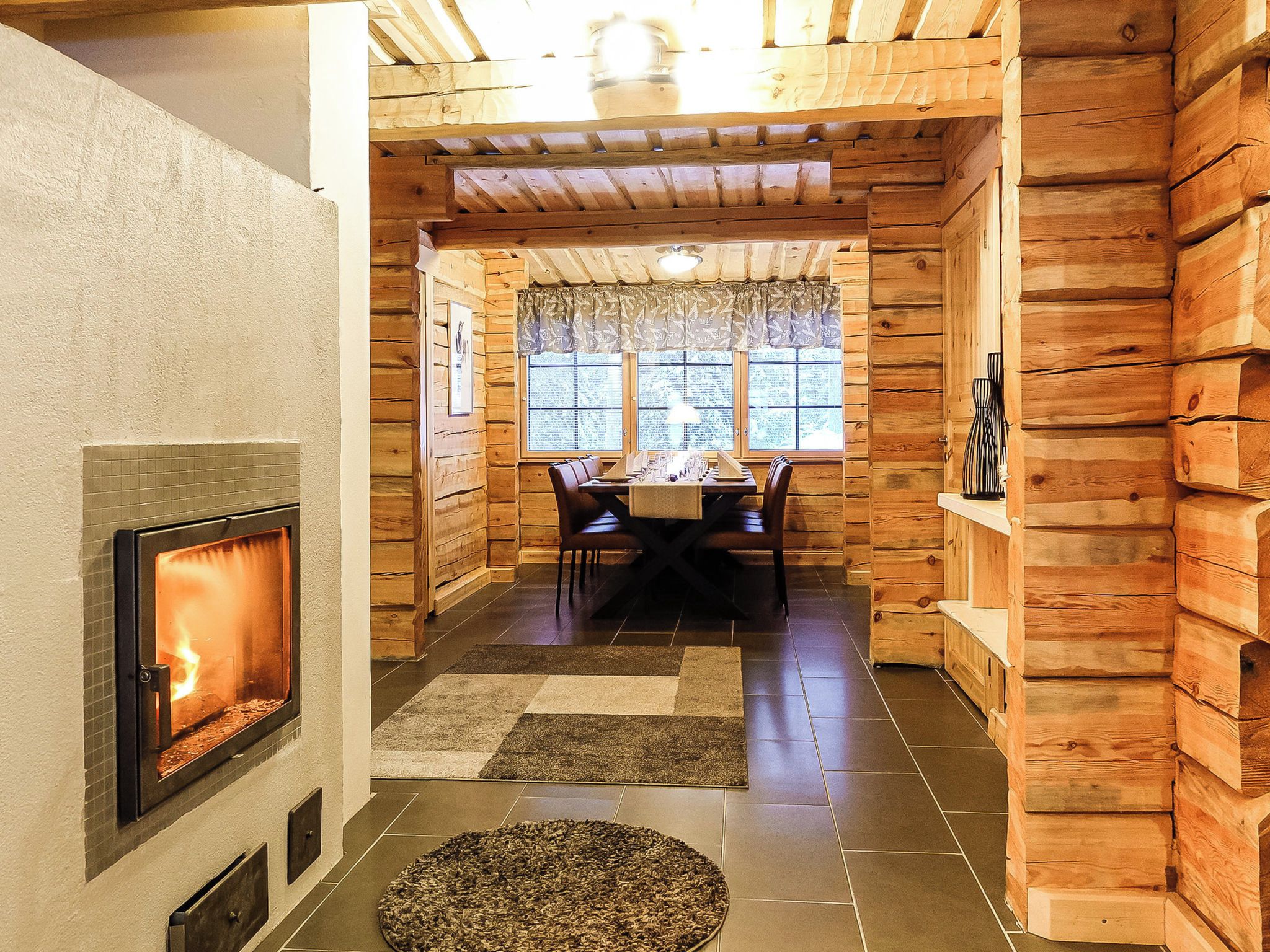A log cabin interior with a fireplace, a dining area, and a window with curtains.