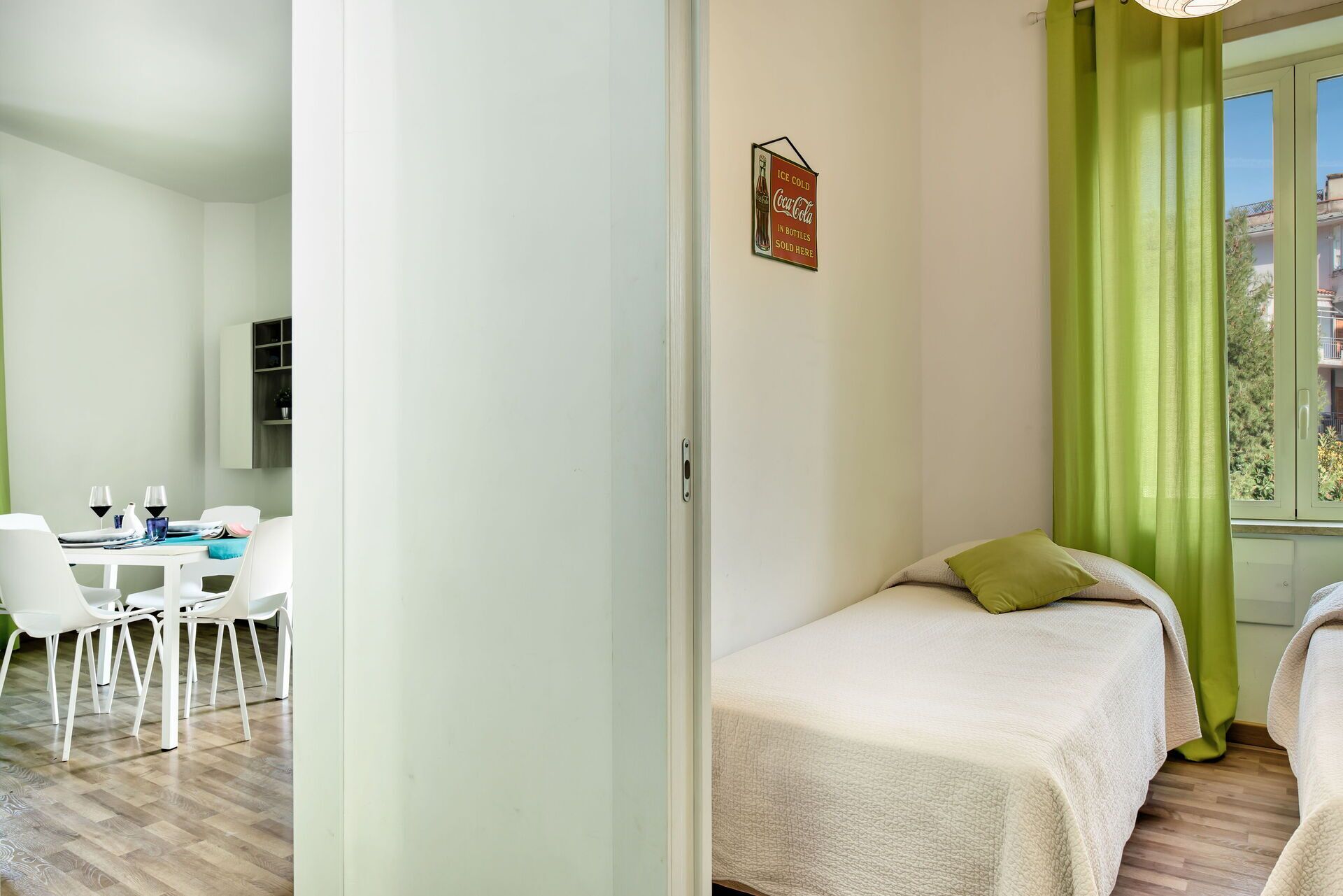 Una habitación con una cama, una mesa de comedor con sillas y un ventanal con cortinas verdes.