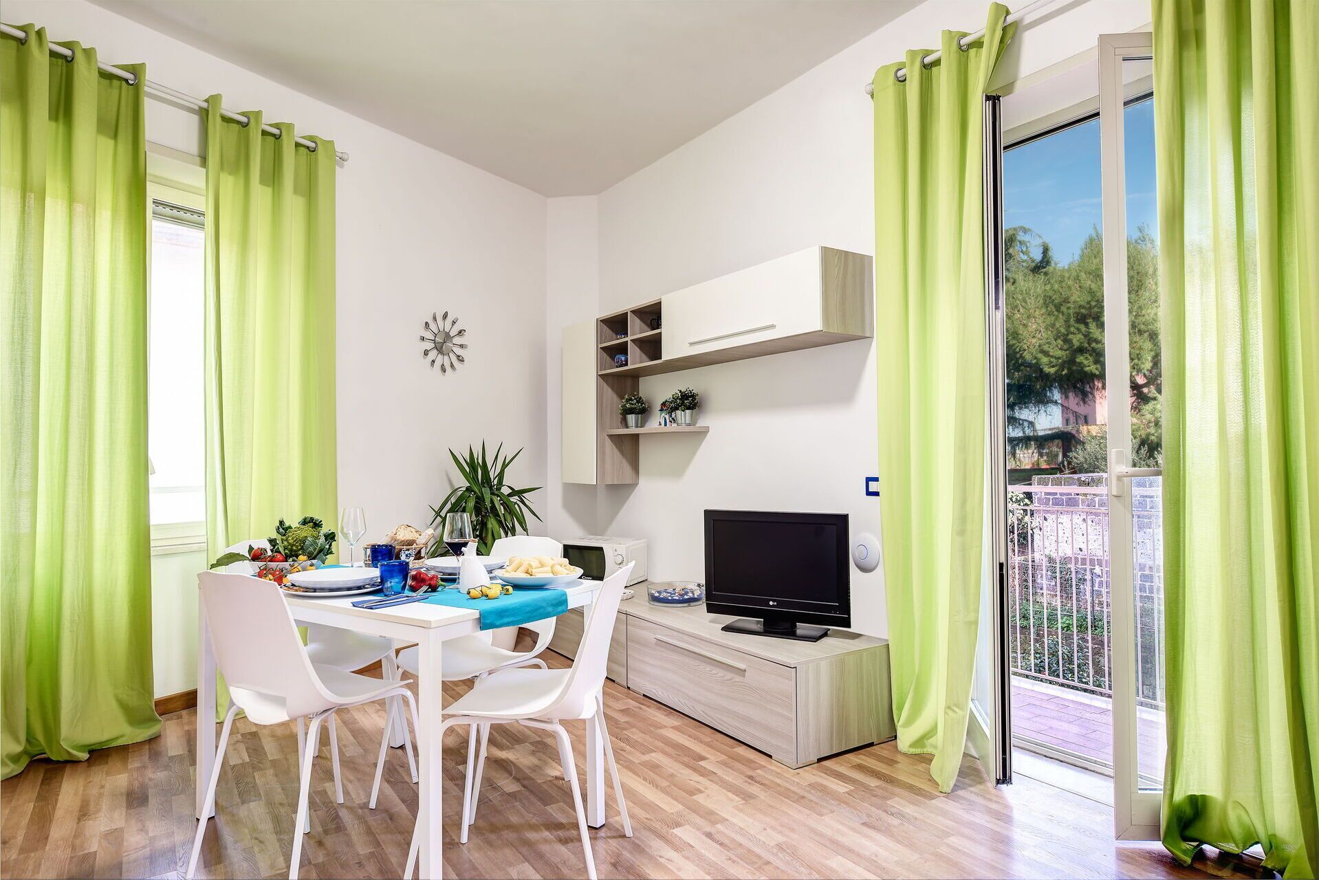 A dining area with a table set for two, a TV, and a small cabinet.