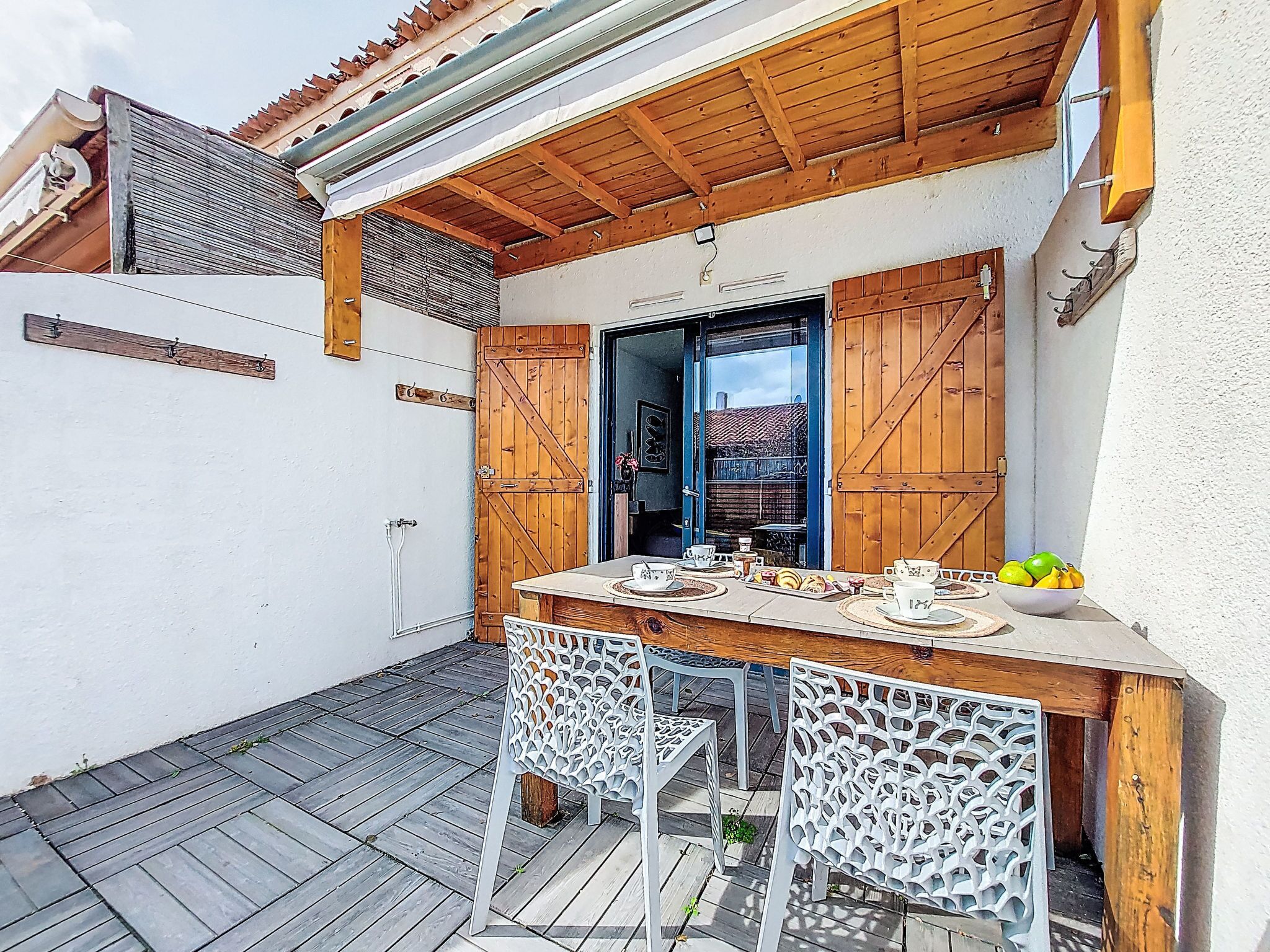 A patio with a wooden table, white chairs, and a bowl of fruit.