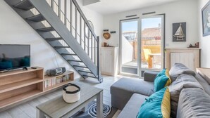 Ett modernt vardagsrum med en trappa, en tv, en bokhylla och en soffa med kuddar.
