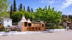 A brick-built outdoor structure with multiple chimneys, surrounded by lush greenery and a paved area.