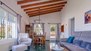 A spacious living area with a high ceiling, a dining table, a sofa, and a window with curtains.
