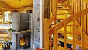 Interior acogedor de una cabaña con chimenea de piedra, escalera de madera y comedor con banco y mesa.