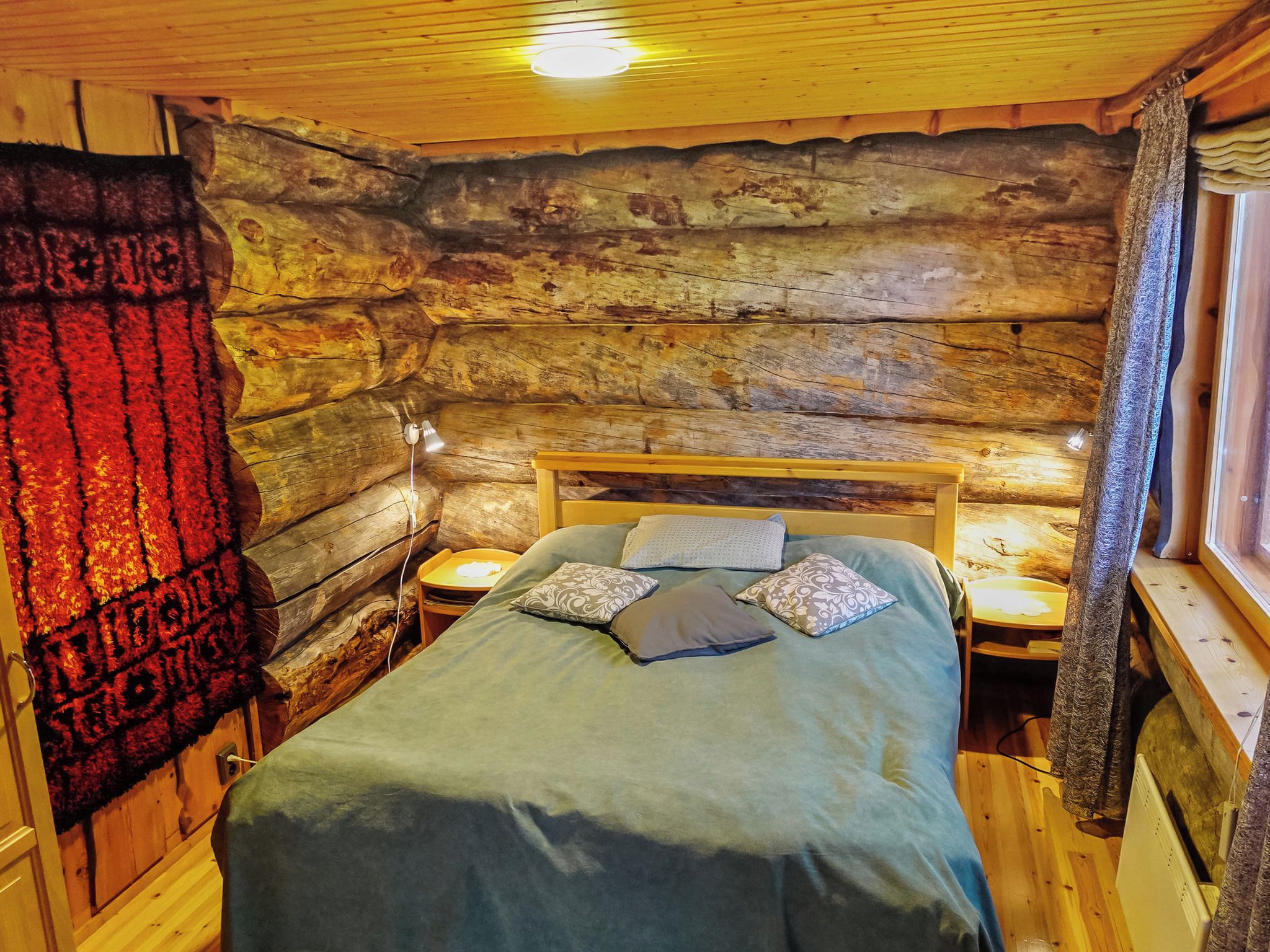 A cozy log cabin room with a bed, bedside tables, and a window with curtains.