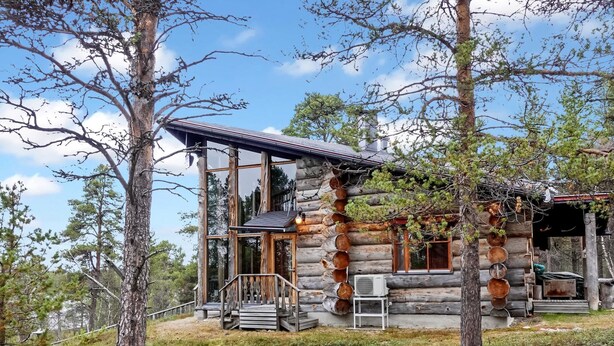 Una cabaña de troncos con terraza de madera, ventanas grandes y porche cubierto.