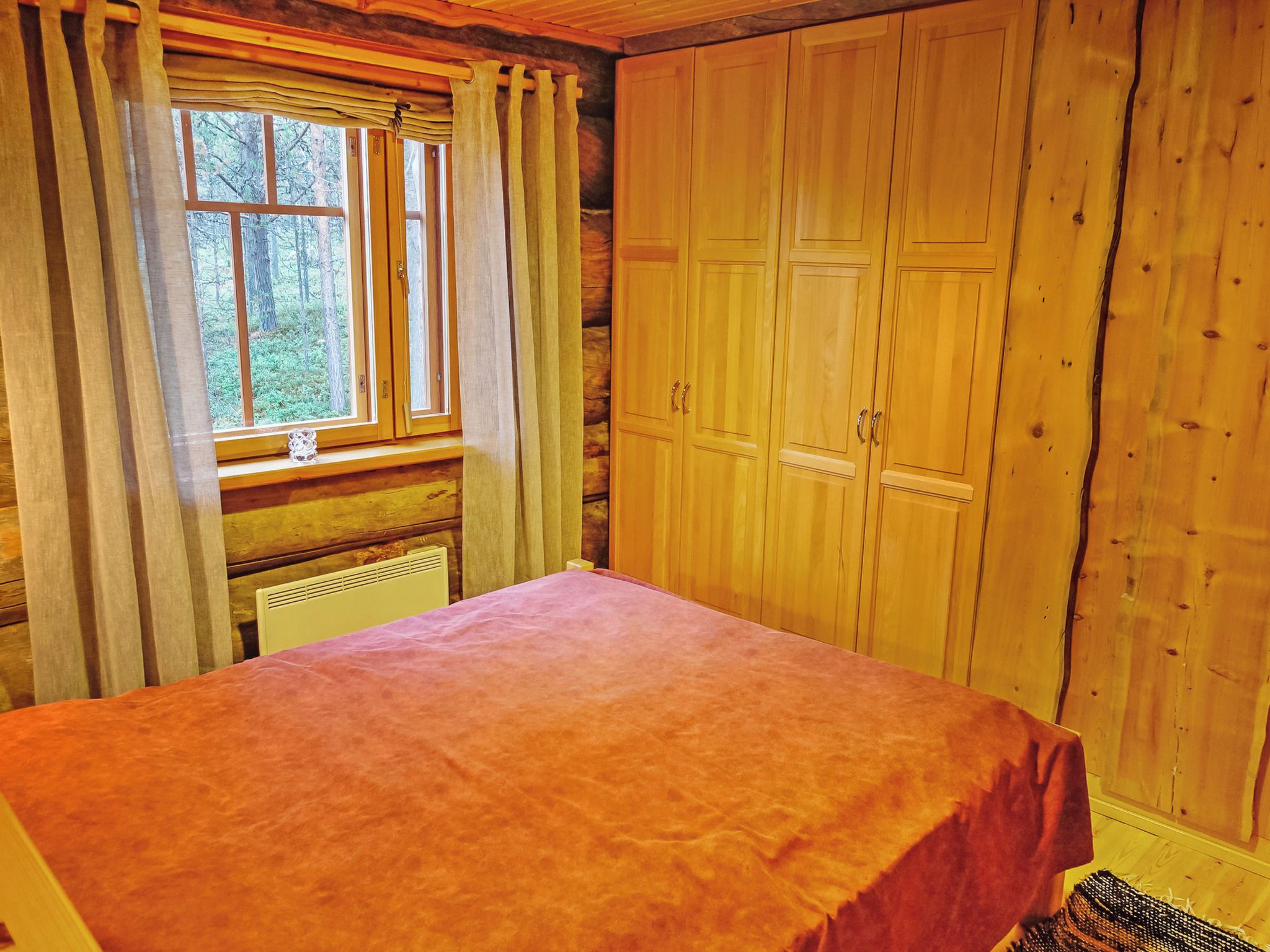 A room with a bed, wooden wardrobe, and a window with curtains.