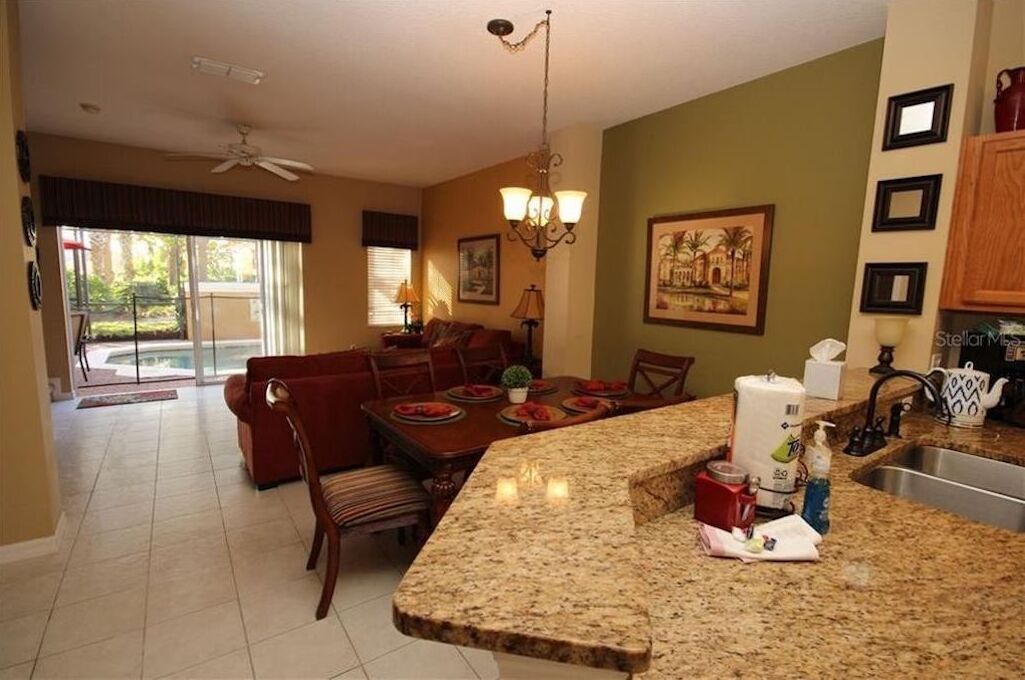 A spacious kitchen with granite countertops, a dining area with a red sofa, and a large window offering a view of the outdoors.