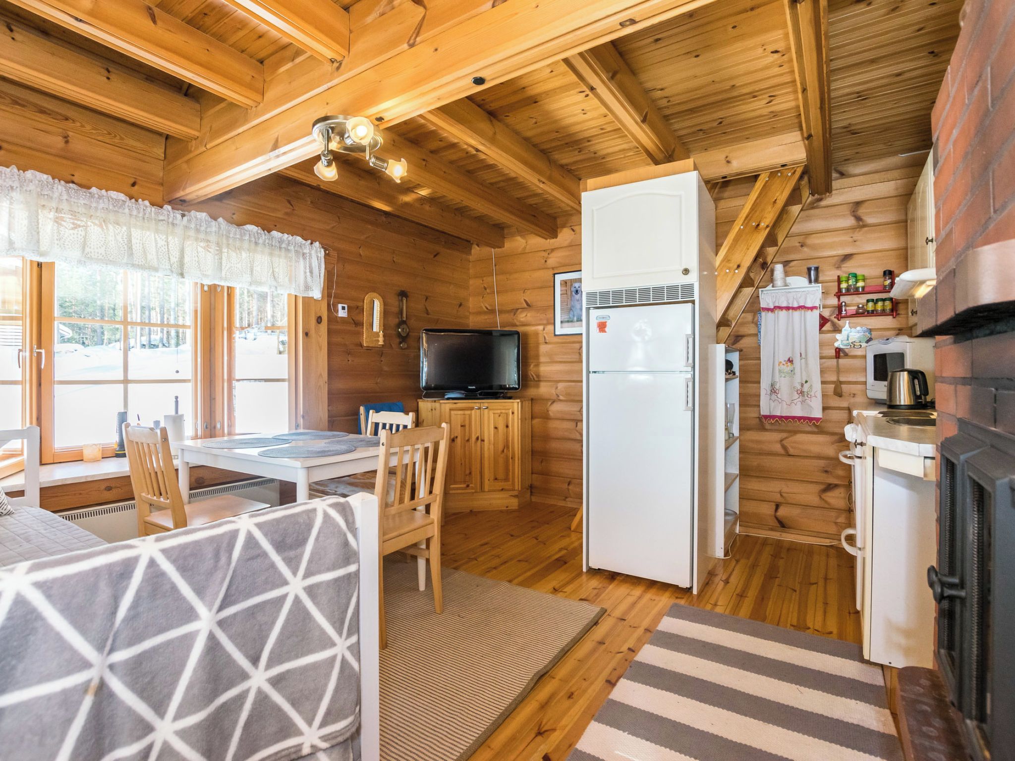 A cozy cabin interior with a dining area, a kitchen with a refrigerator and stove, and a television.