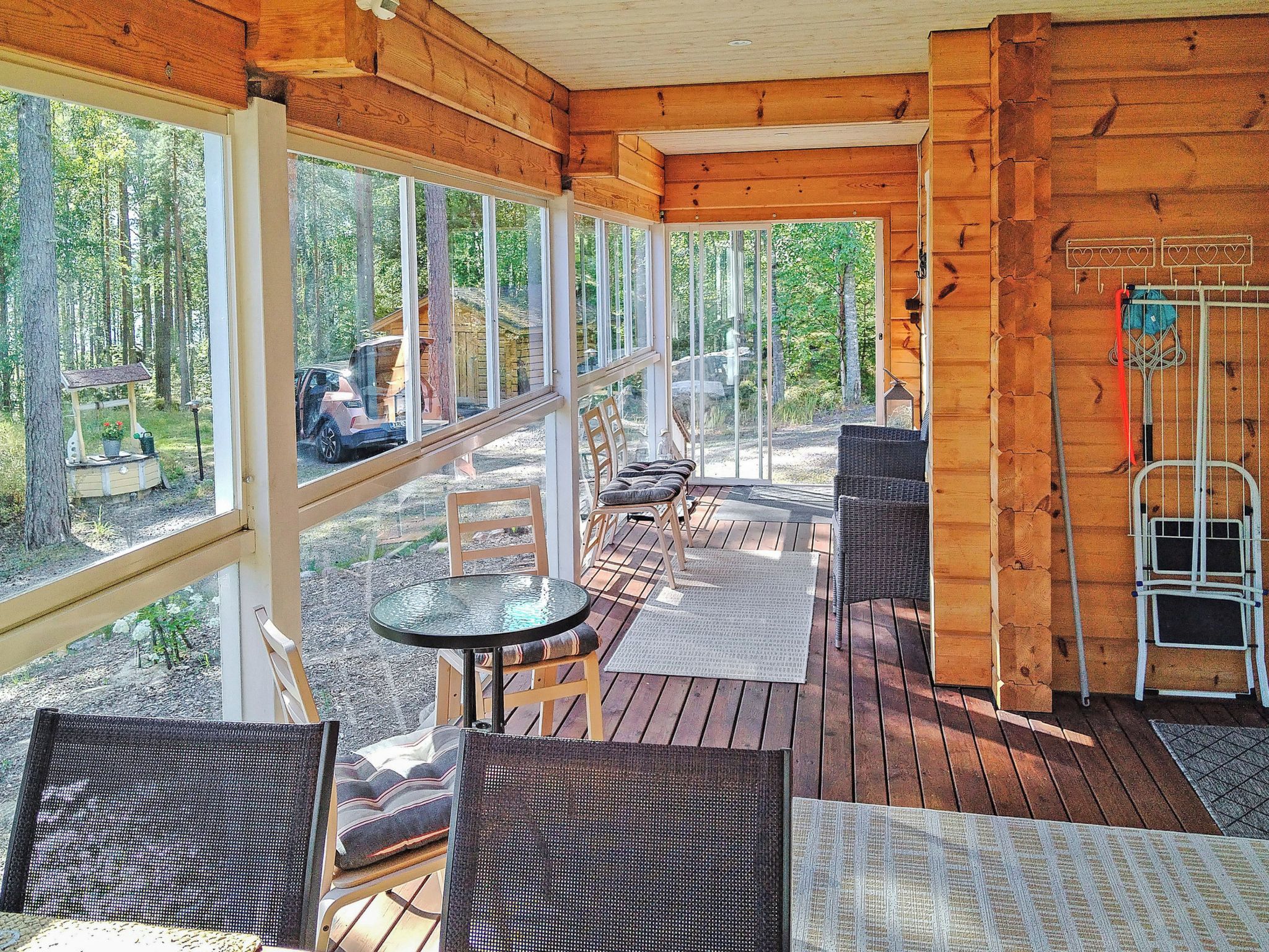 Una terraza de madera con mobiliario exterior, ventanas amplias y vista al bosque.