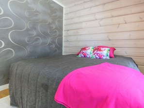 Een slaapkamer met een grijze sprei, een roze deken en een kleurrijk kussen.