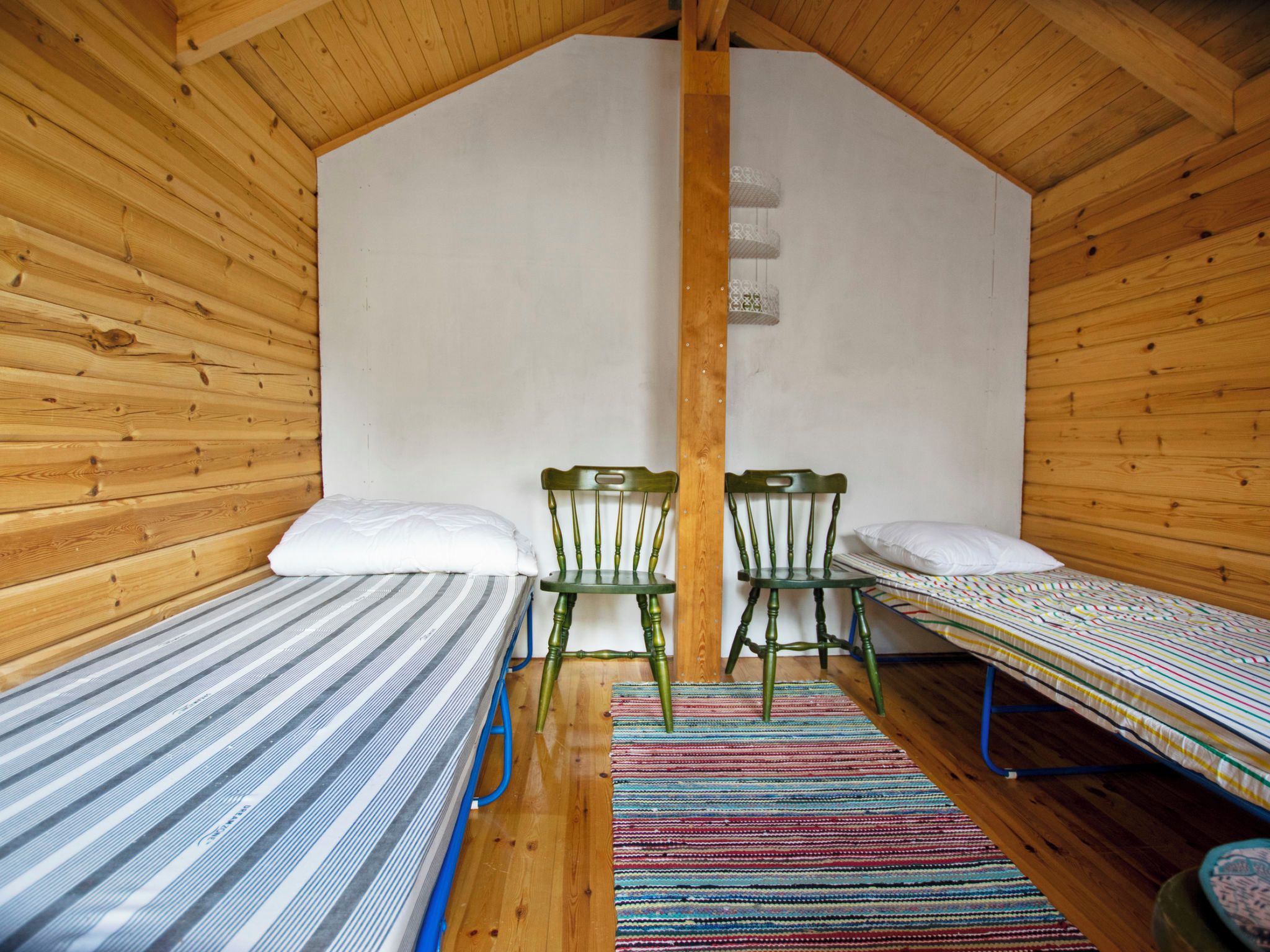 Une petite pièce agréable et chaleureuse, avec deux lits simples, un plafond en bois et un simple mur en bois.