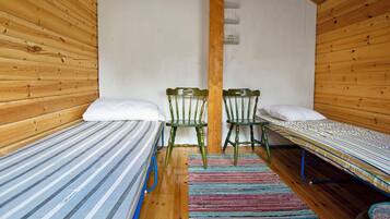 Une petite pièce agréable et chaleureuse, avec deux lits simples, un plafond en bois et un simple mur en bois.