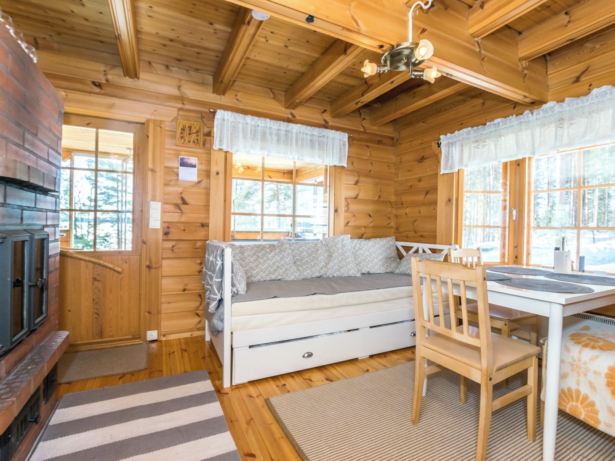 Ein gemütliches Blockhaus-Interieur mit Kamin, einer Couch, einem Esstisch und großen Fenstern.