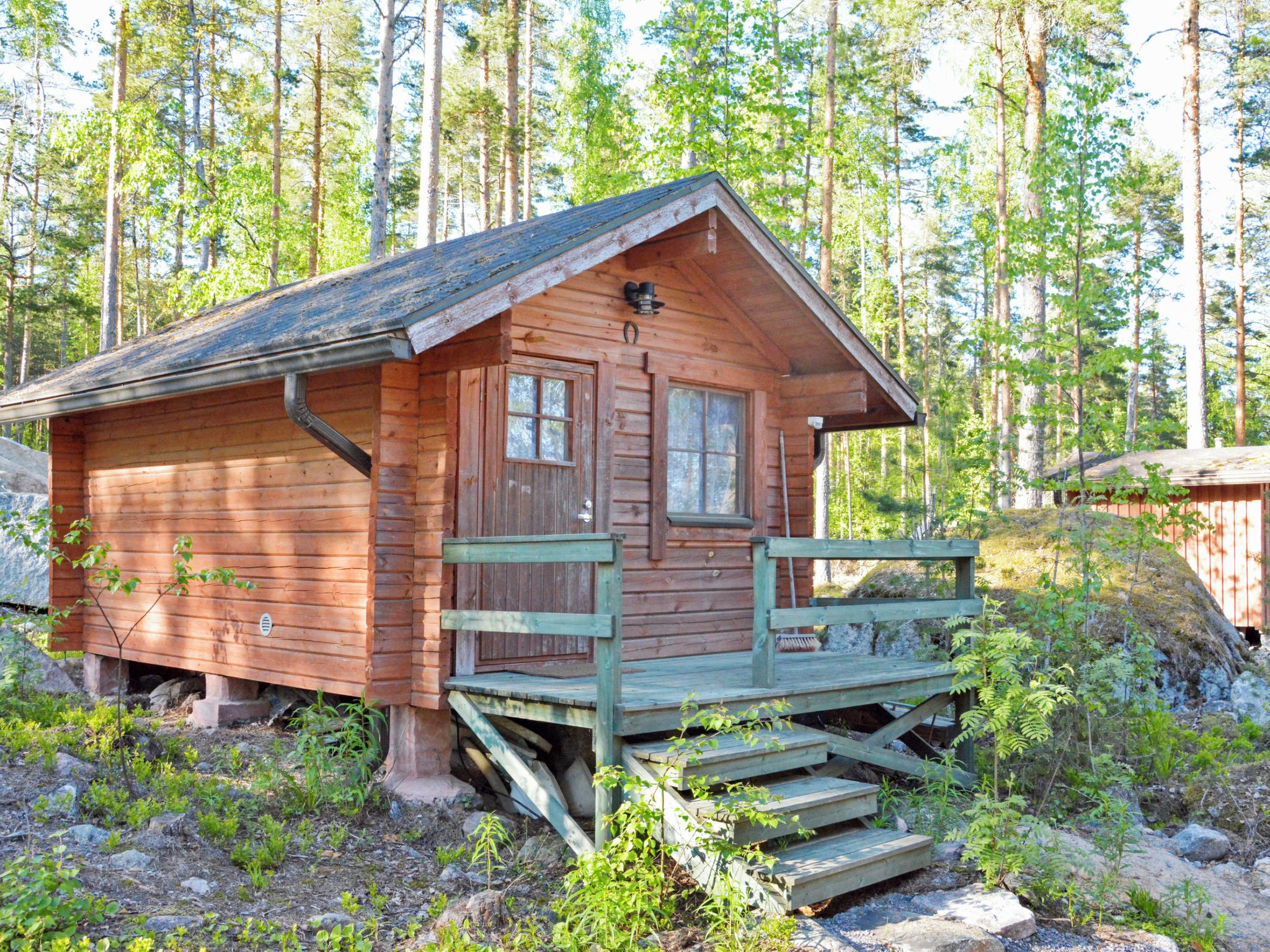 Eine Holzhütte mit Veranda und kleinem Fenster, umgeben von Bäumen.