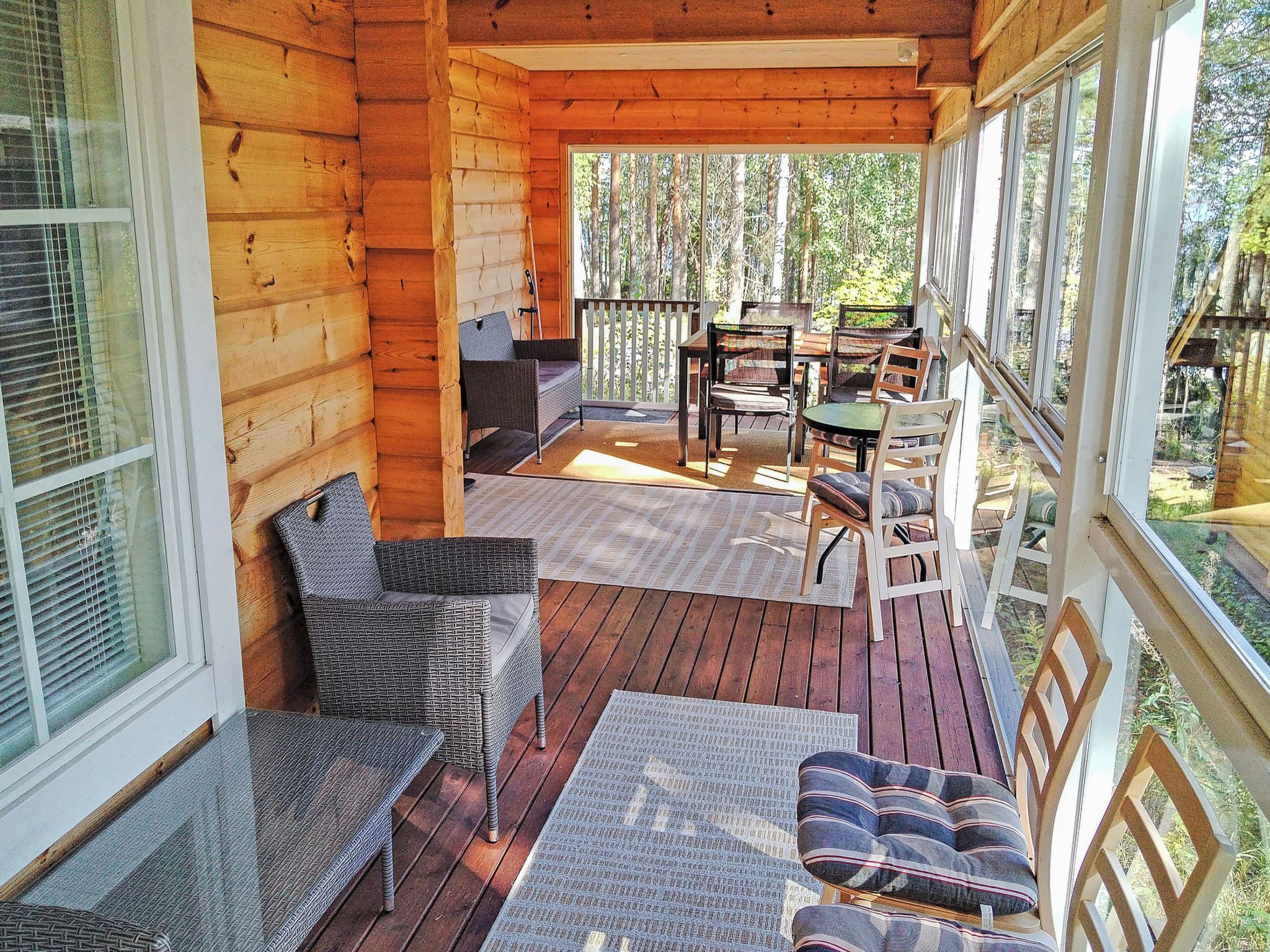 A wooden deck with outdoor furniture, including chairs and a table, overlooking a forested area.