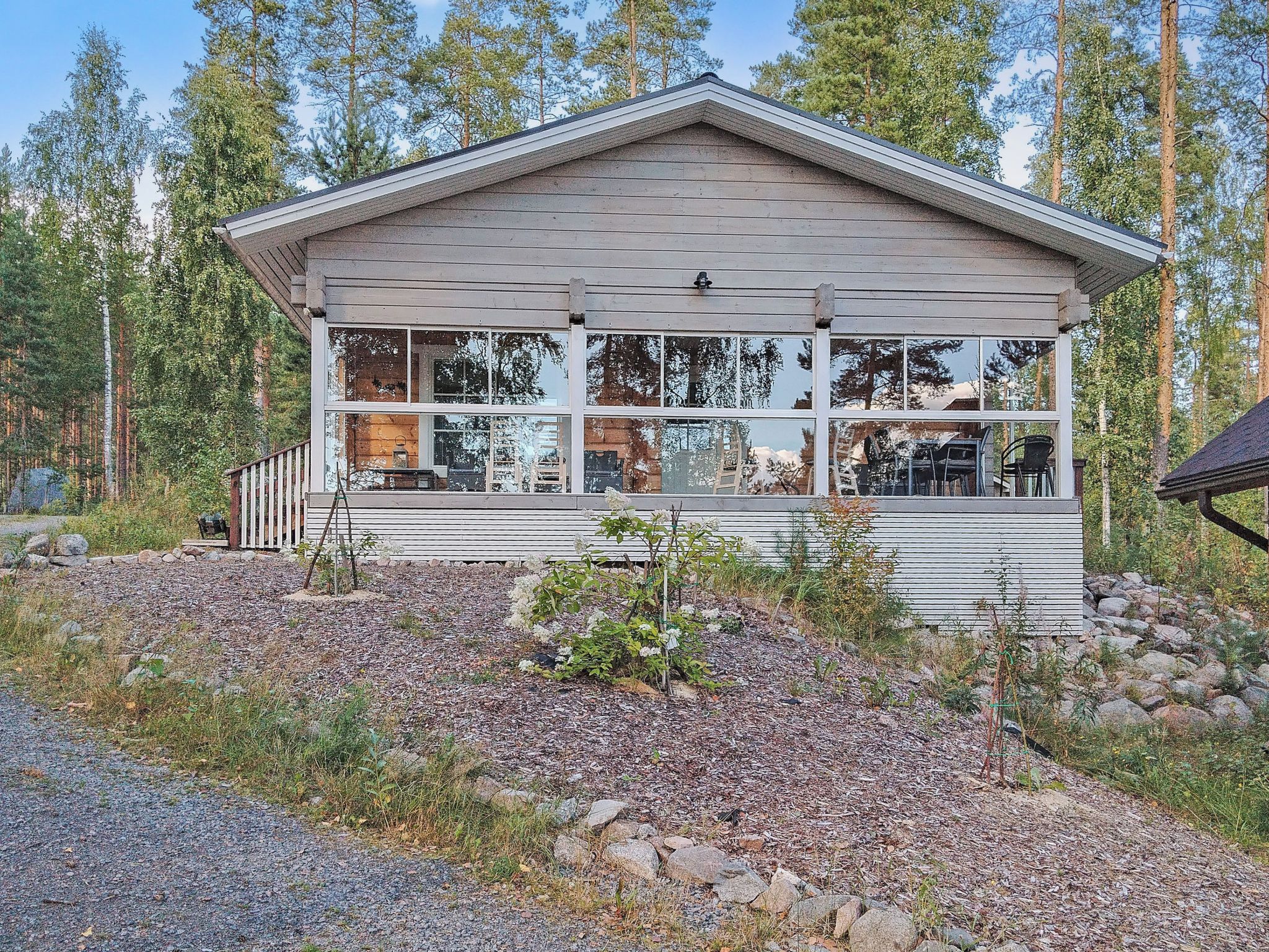 A cabin with a porch, large windows, and a view of the surrounding forest.