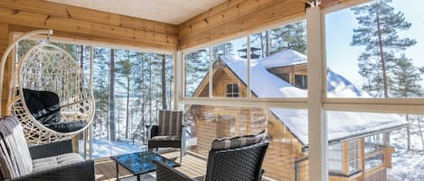 A wooden deck with wicker furniture and a hanging chair, overlooking a snowy mountain cabin.