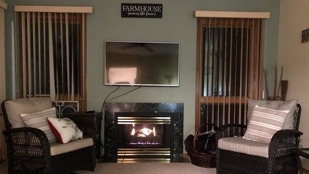 Un salon avec deux fauteuils en osier, une cheminée et un téléviseur fixé au mur.