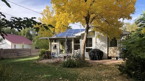 Une maison avec un toit équipé de panneaux solaires, un espace extérieur aménagé avec des sièges et un jardin parsemé de feuilles mortes.