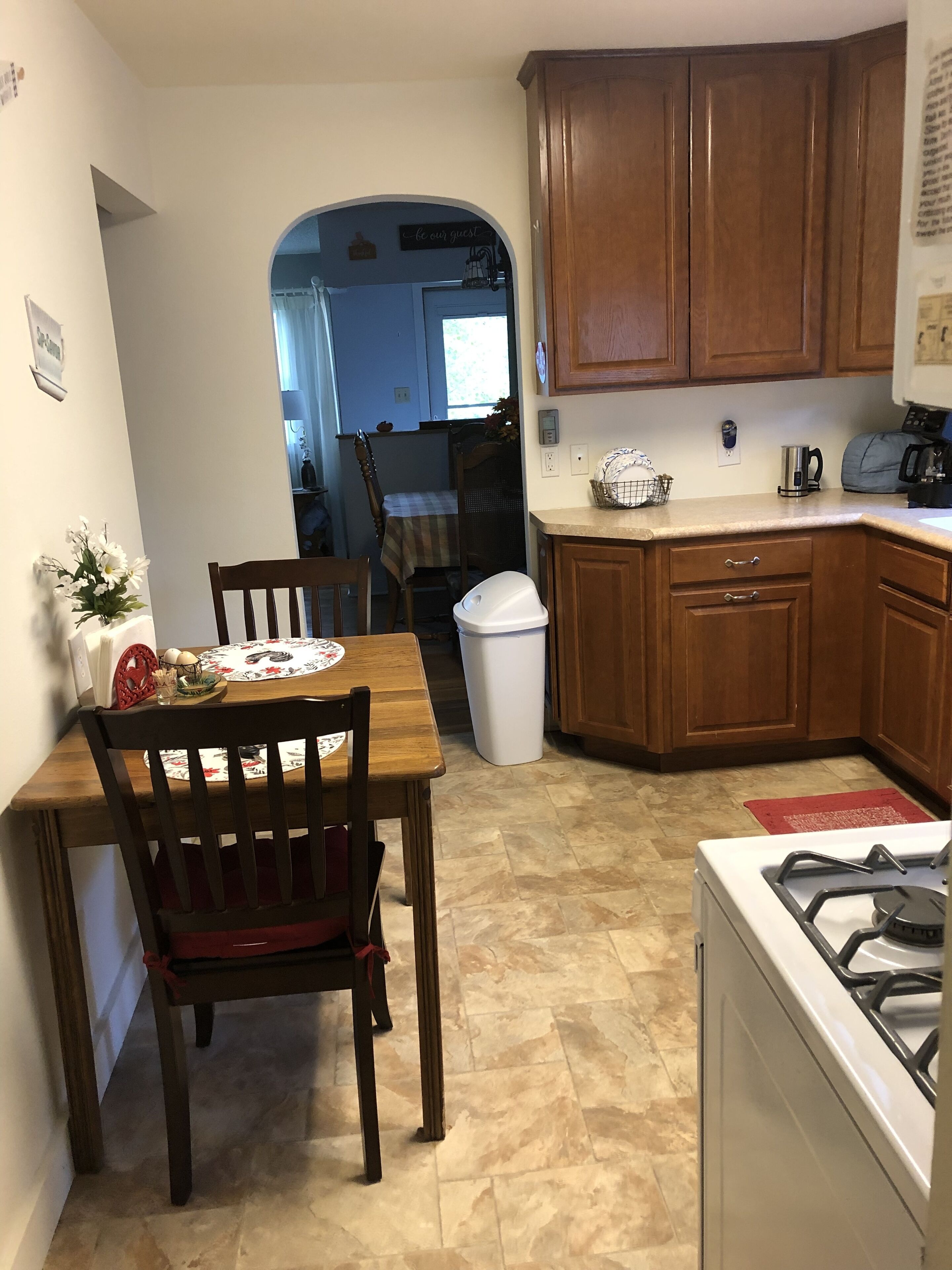 A kitchen with wooden cabinets, a gas stove, a trash can, and a dining table with chairs.