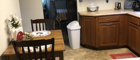 A kitchen with wooden cabinets, a gas stove, a trash can, and a dining table with chairs.