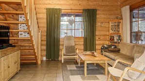 A cozy log cabin interior with a wooden staircase, a dining area, a sofa, and a television.