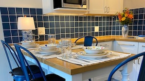 A dining area with a table set for four, blue chairs, a microwave above the table, and a tiled backsplash. - Luxury Retreat in Prime Downtown Spring Green Location  (Spring Green)