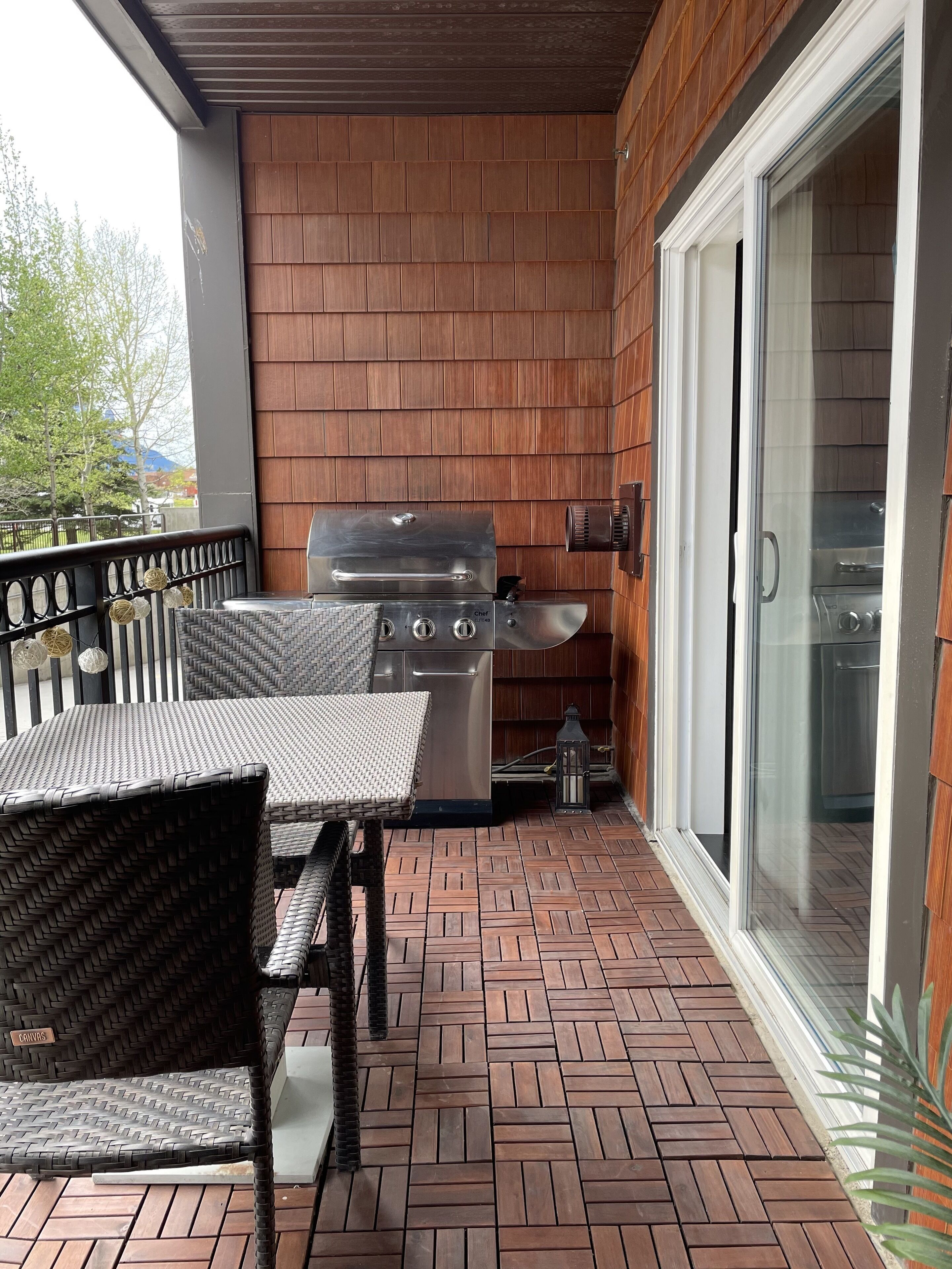 A covered patio with a grill, wicker furniture, and a brick floor.