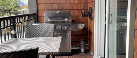 A covered patio with a grill, wicker furniture, and a brick floor.