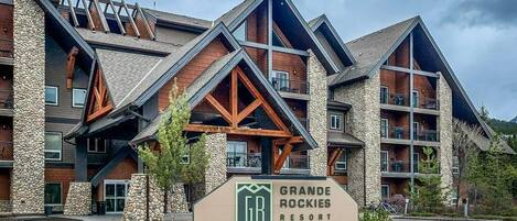 Ein mehrstöckiges Gebäude mit einer Steinfassade, einem markanten Schild für das Grande Rockies Resort und einem Parkplatz.
