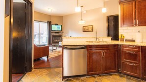 A modern kitchen with granite countertops, stainless steel dishwasher, wooden cabinets, and pendant lighting.