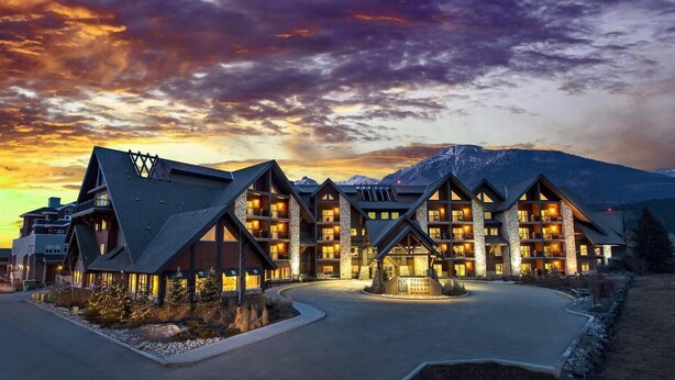 A lodge with multiple floors and a prominent entrance, surrounded by mountains and a sunset sky.