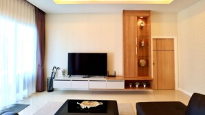 A modern living room with a flat-screen TV, wooden cabinet, and two black sofas. - Luxury Pool Villa A10  (Bang Lamung)