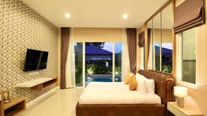A bedroom with a large bed, a TV mounted on the wall, and a view of a swimming pool and building outside. - Luxury Pool Villa A10  (Bang Lamung)