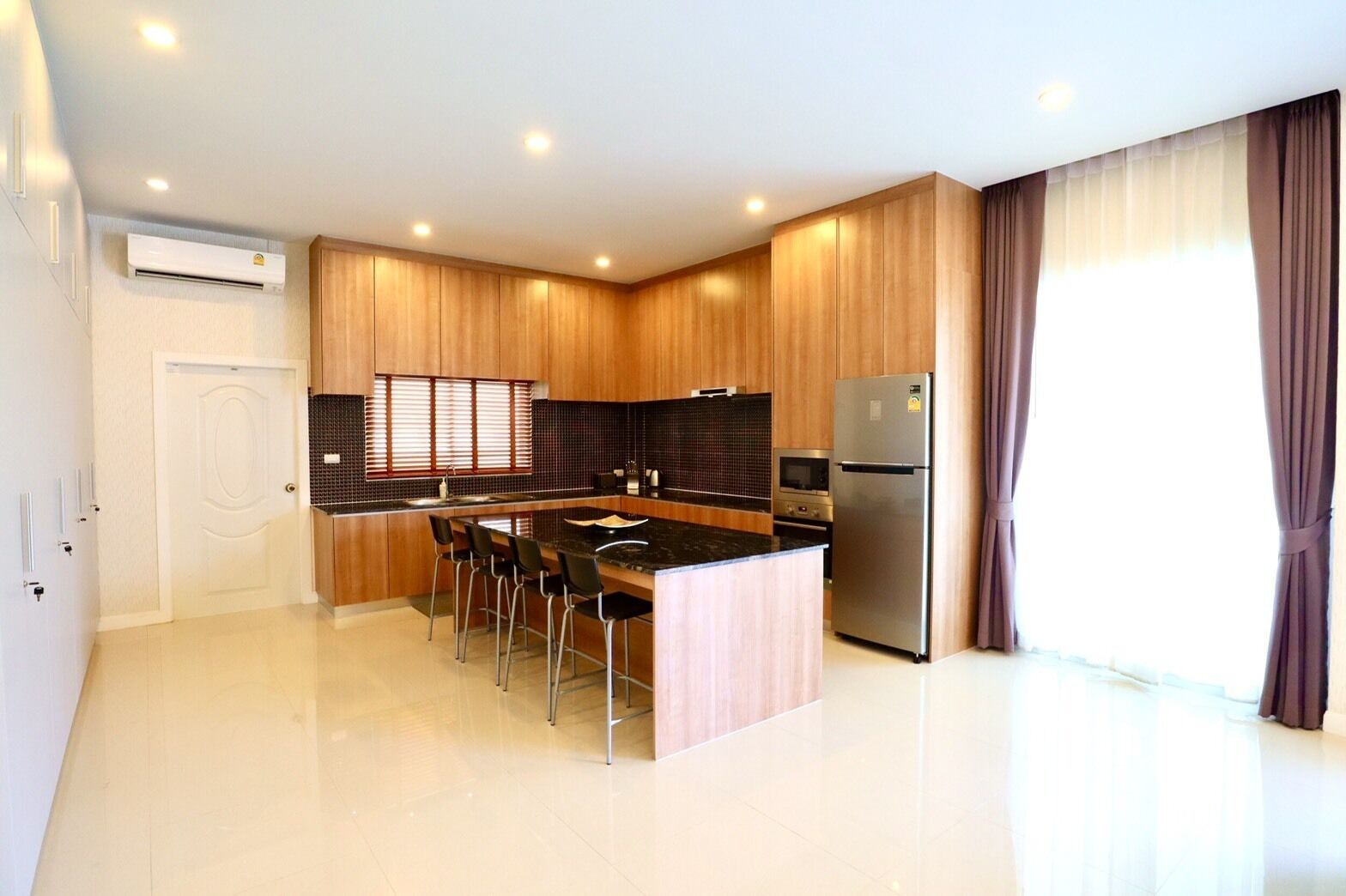 A modern kitchen with a central island, stainless steel appliances, and a large window with curtains.