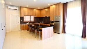 A modern kitchen with a central island, stainless steel appliances, and a large window with curtains. - Luxury Pool Villa A10  (Bang Lamung)