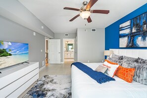 Une chambre à coucher moderne, dotée d’une télévision, d’un ventilateur de plafond et d’œuvres d’art accrochées au mur.
