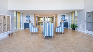 A spacious lobby with a tiled floor, striped armchairs, a round table, and a potted plant. - Oceanfront-Pool-Aruba #905-EV Charging (Daytona Beach Shores)