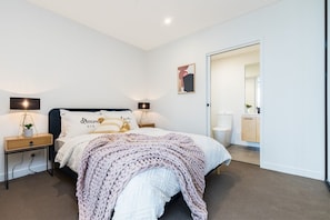 Cozy retreat with a neatly made bed, nightstand, and potted plant.