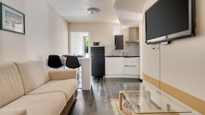 A modern living room with a sofa, a glass coffee table, and a TV mounted on the wall.