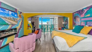 Quarto de hotel com cama, escrivaninha, cadeira e vista para a praia.